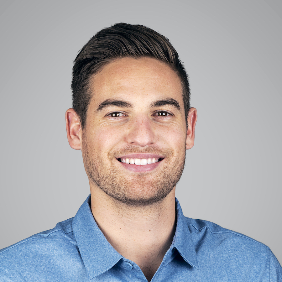 Smiling man in a blue shirt with brown hair and light beard, against a gray background.