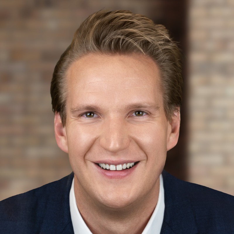 Professional headshot of a smiling man with light brown hair and green eyes in a blue suit.