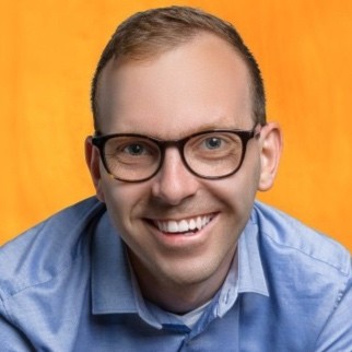 Smiling man with glasses in a blue shirt on an orange background.