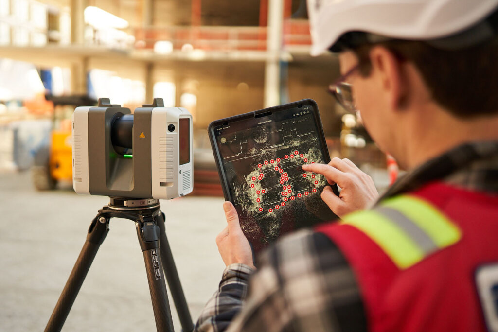 Construction worker uses a reality capture laser scanner with a tablet showing scan data on site.