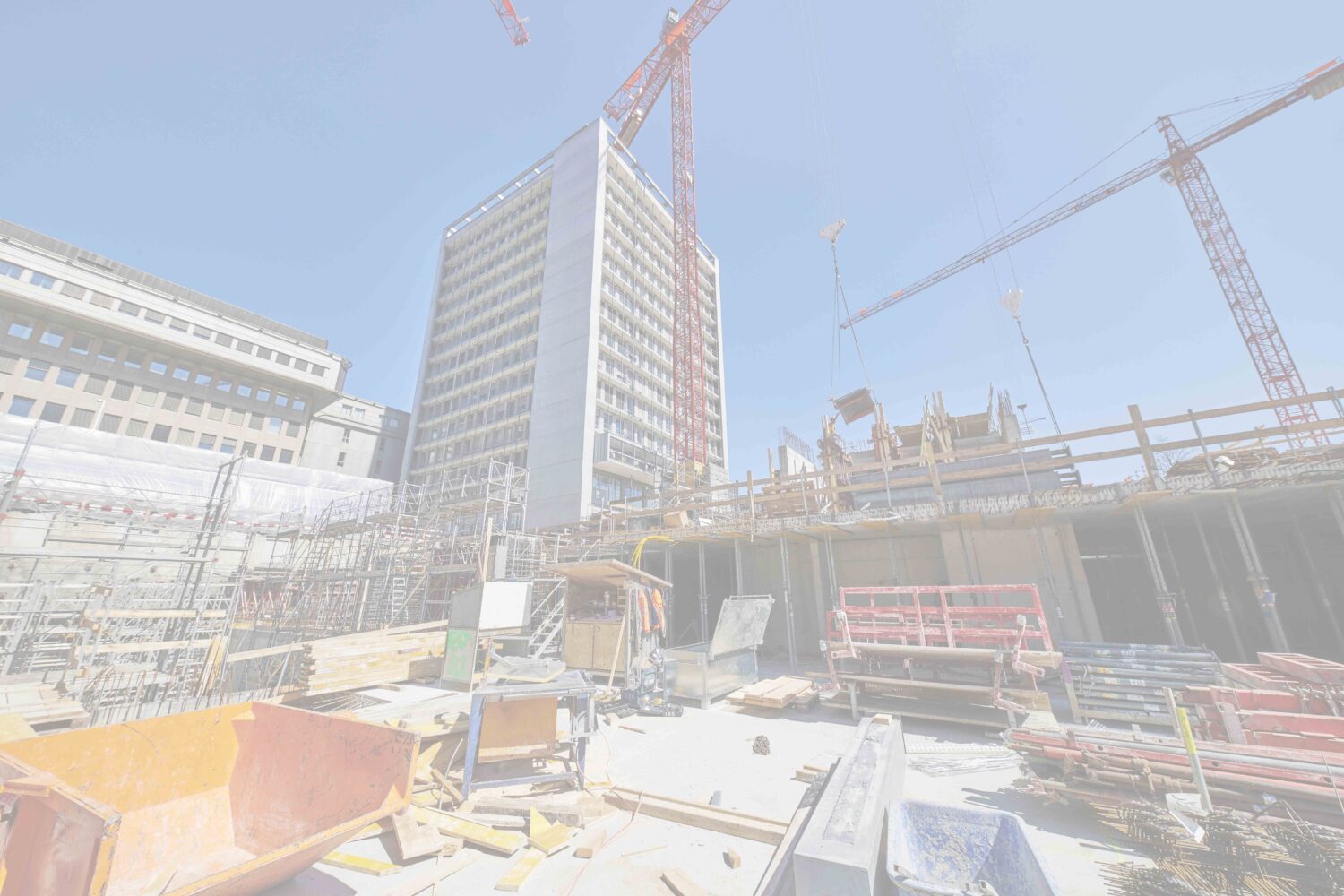 Large urban construction site with a tall building under development, multiple cranes, scaffolding, and materials.