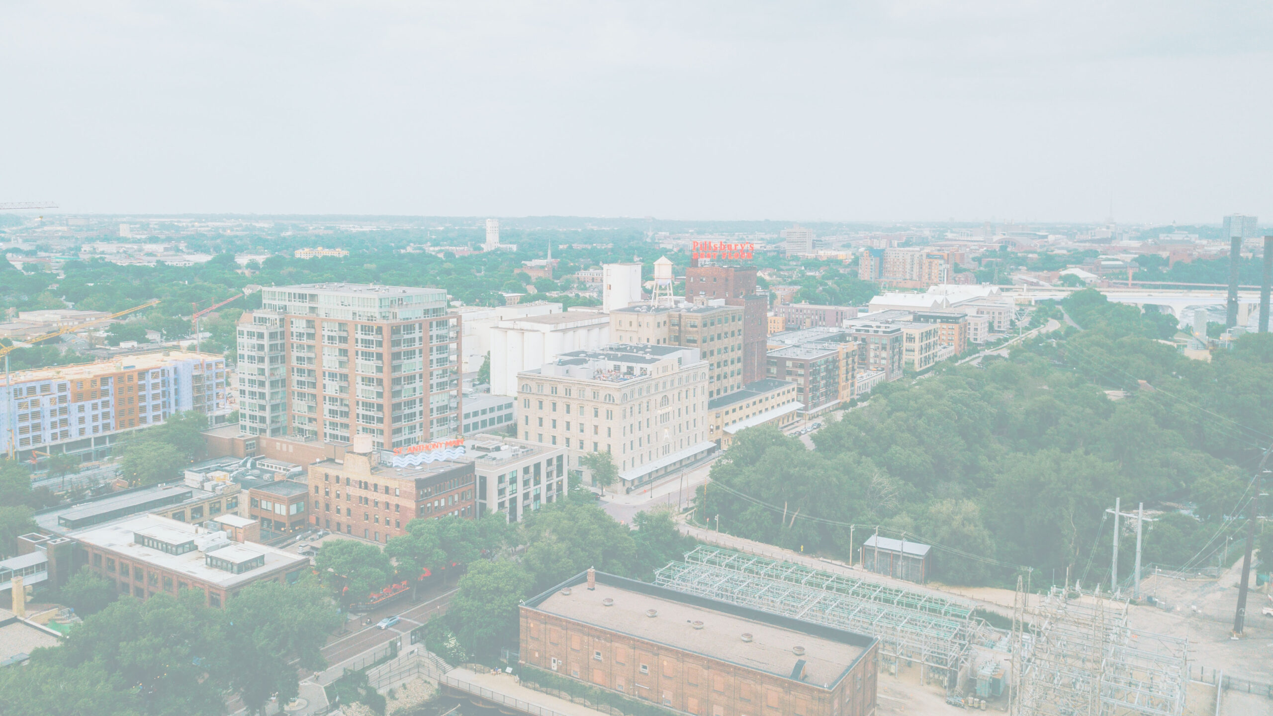 Aerial cityscape featuring a mix of modern and historic buildings, green spaces, and the iconic Pillsbury sign on a rooftop.