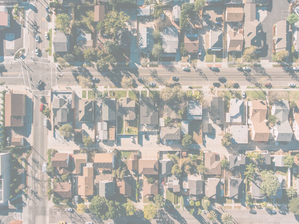 Aerial view of a suburban neighborhood with houses, multiple streets, cars, and green trees.