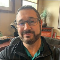 Smiling man with glasses and beard in a casual office setting.