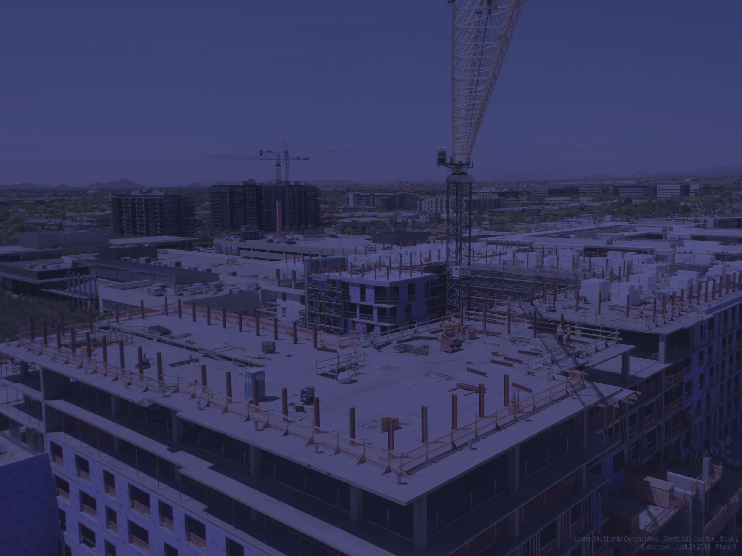 Large building construction site with a towering crane, workers, and a cityscape with mountains.