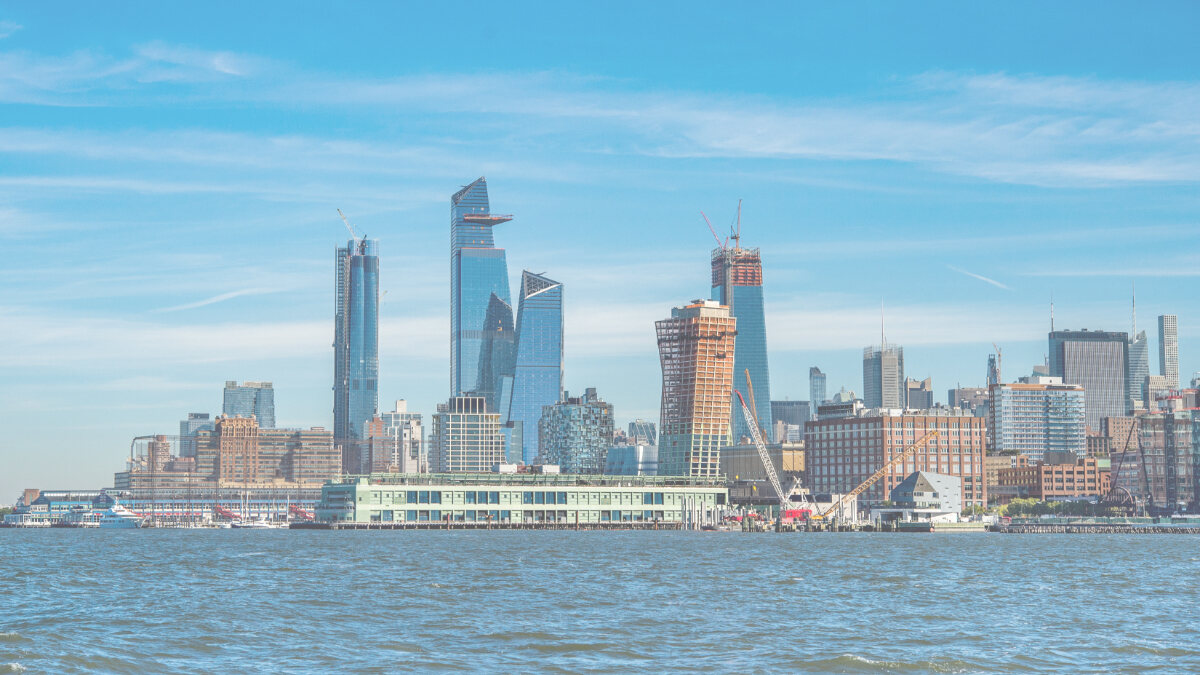 New York City skyline with modern skyscrapers, some under construction, seen across the river on a clear day.