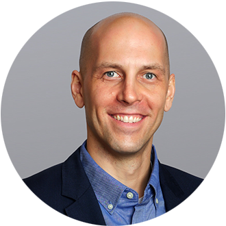 Smiling bald man in a blue shirt and dark blazer.