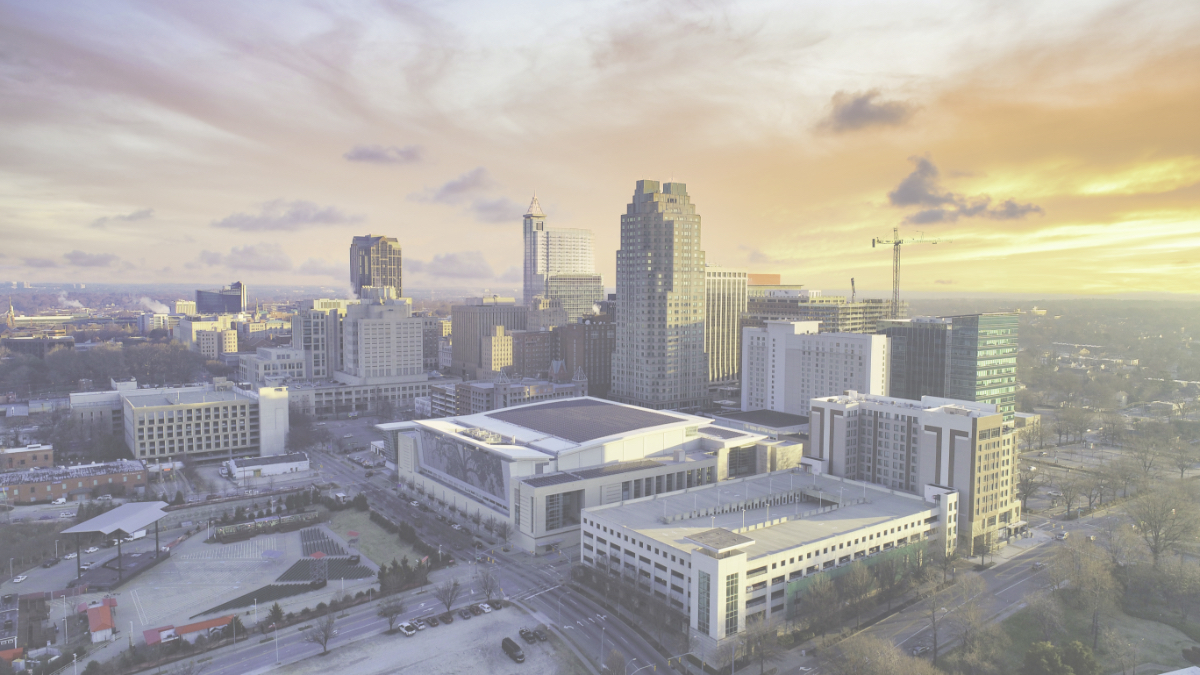 Aerial view of a city skyline at sunset with modern buildings, a large convention center, and an outdoor stage.