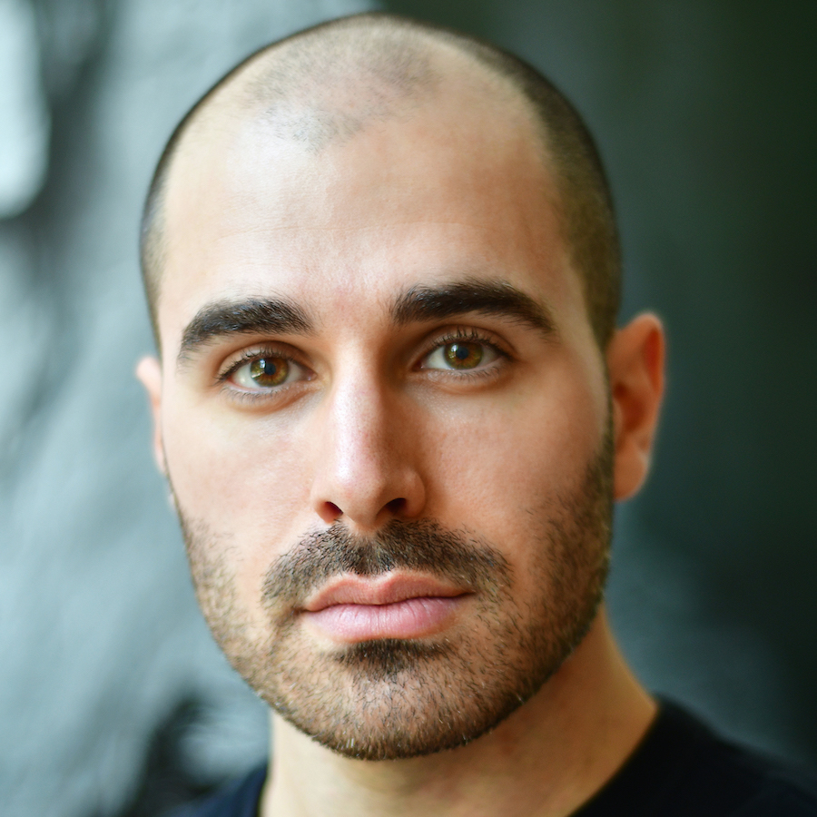 Headshot of a bald man with a beard and striking light brown eyes looking straight ahead.