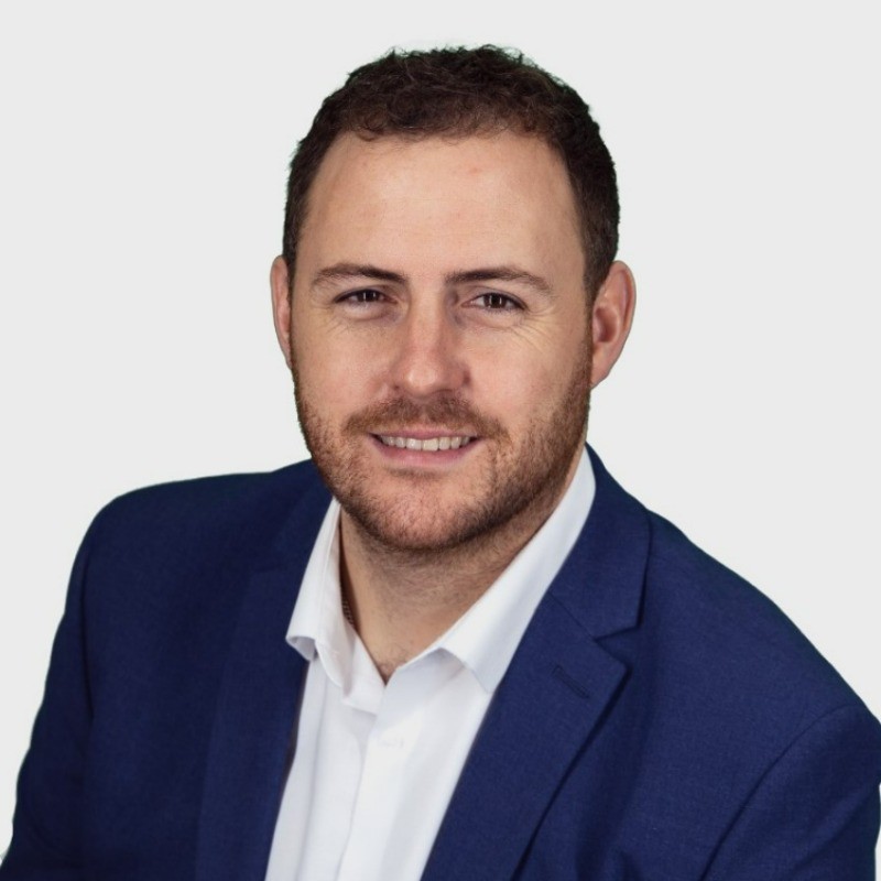 Professional headshot of a smiling man with brown hair and beard in a blue blazer.