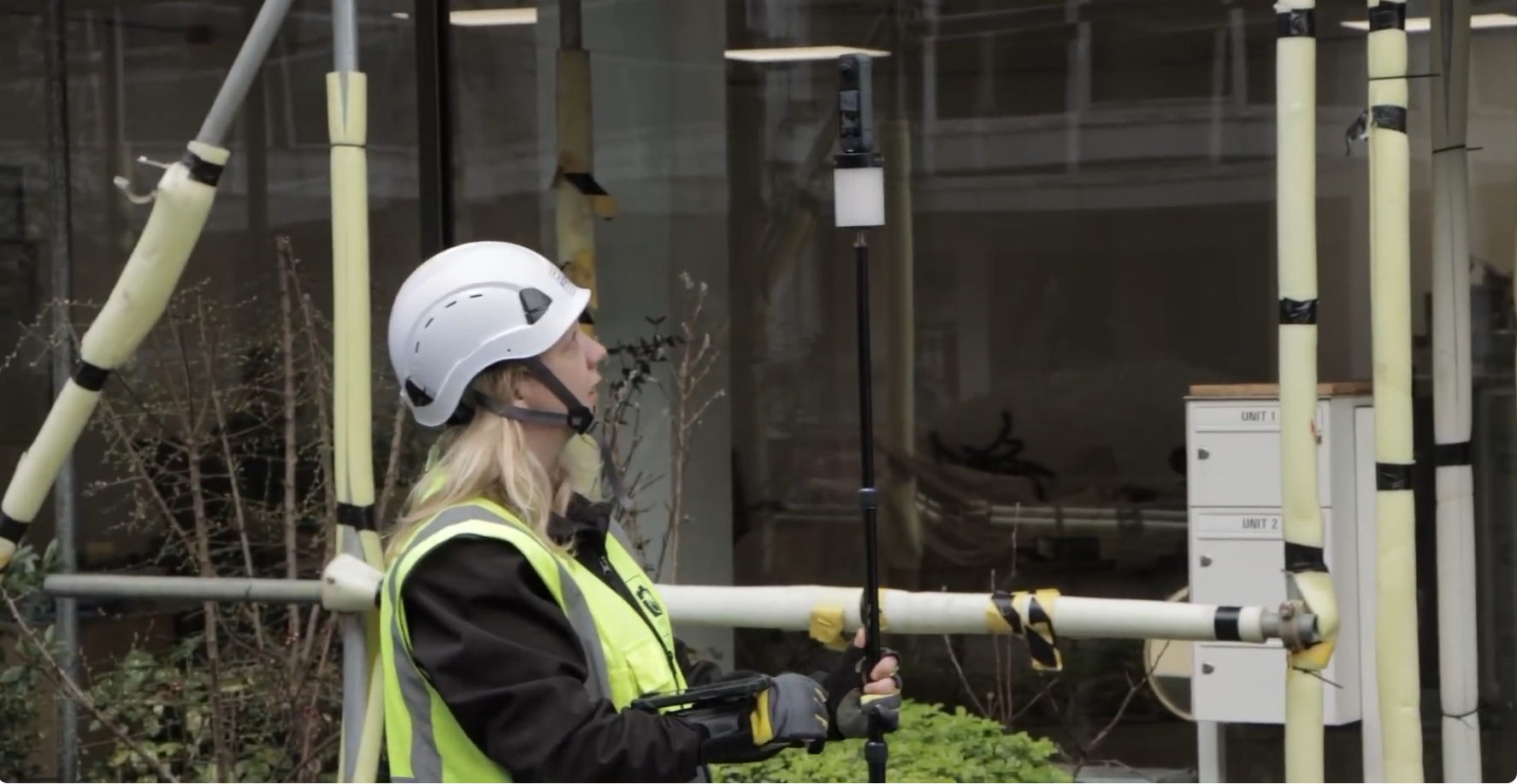 Construction worker in PPE uses a measuring device near scaffolding at a building site.