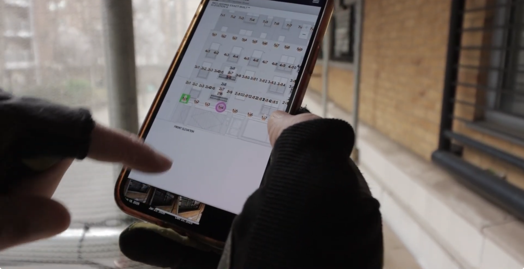Hand uses a smartphone showing a building plan with numbered sections for construction progress.