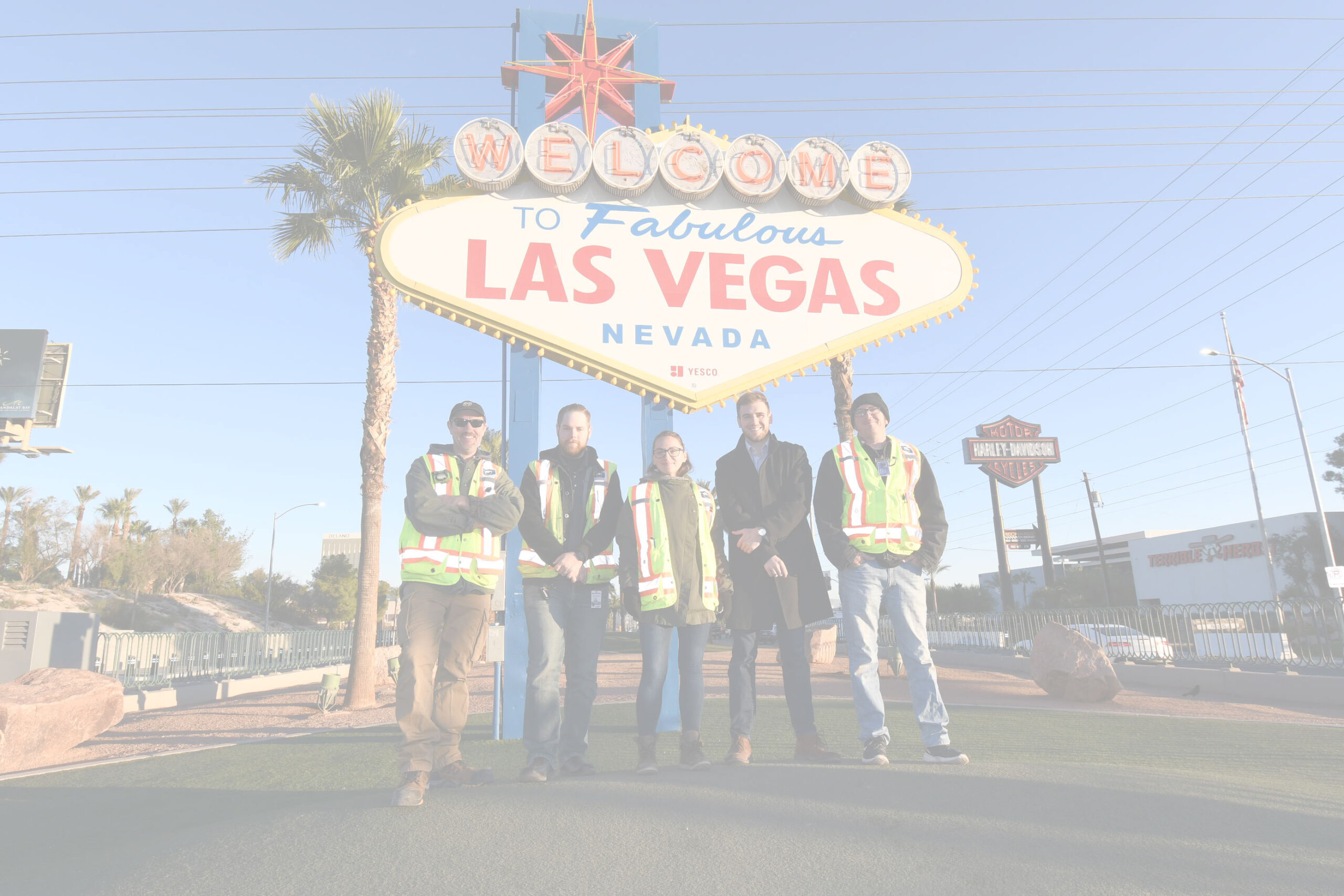 Five people, four in safety vests, smile in front of the iconic Welcome to Fabulous Las Vegas sign.