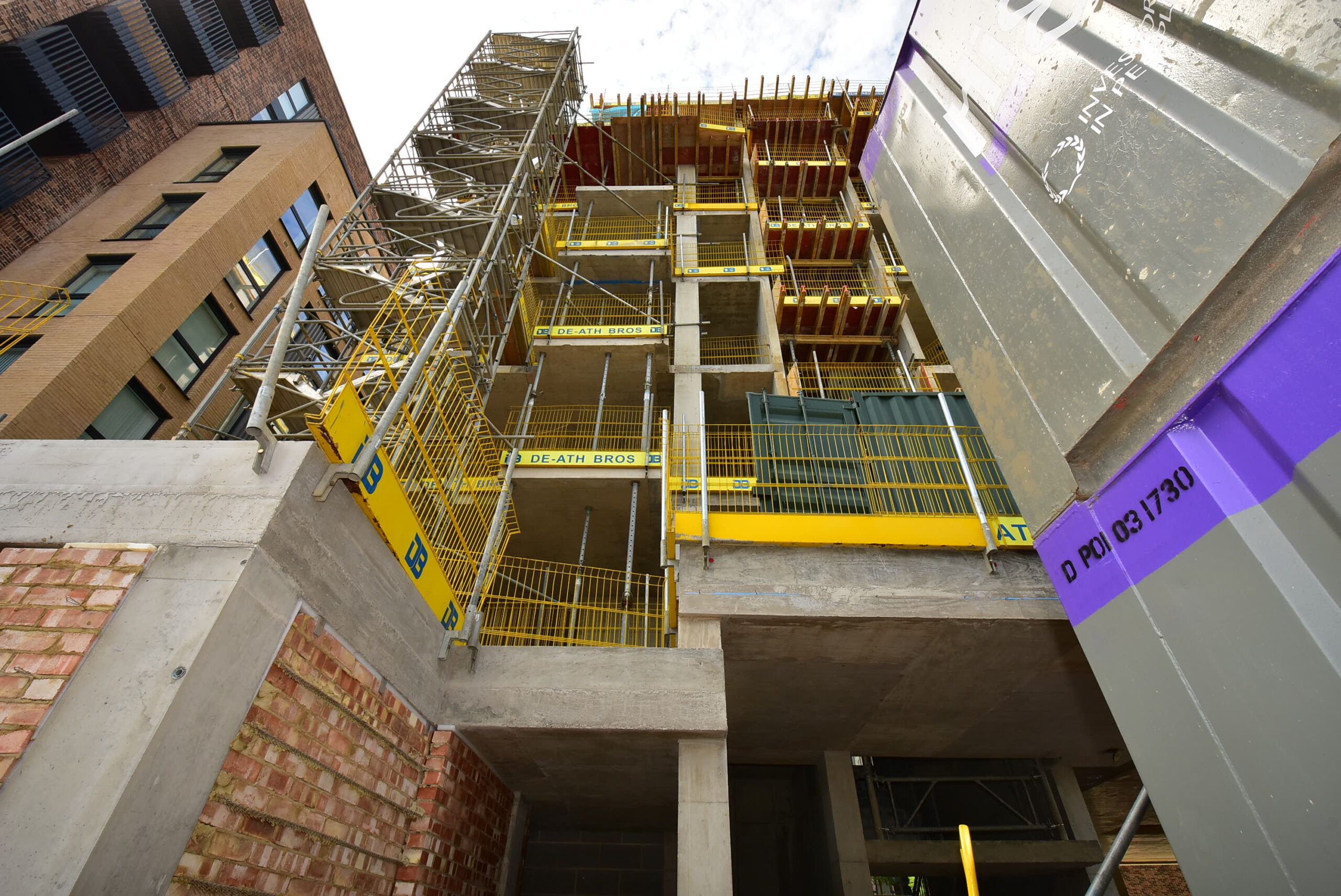 Multi-story building under construction with concrete floors, yellow safety barriers, and scaffolding.