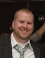 Headshot of a smiling man with short hair and a beard in a suit and striped tie.