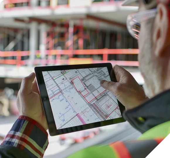 Construction worker in safety gear reviewing building blueprints on a digital tablet.